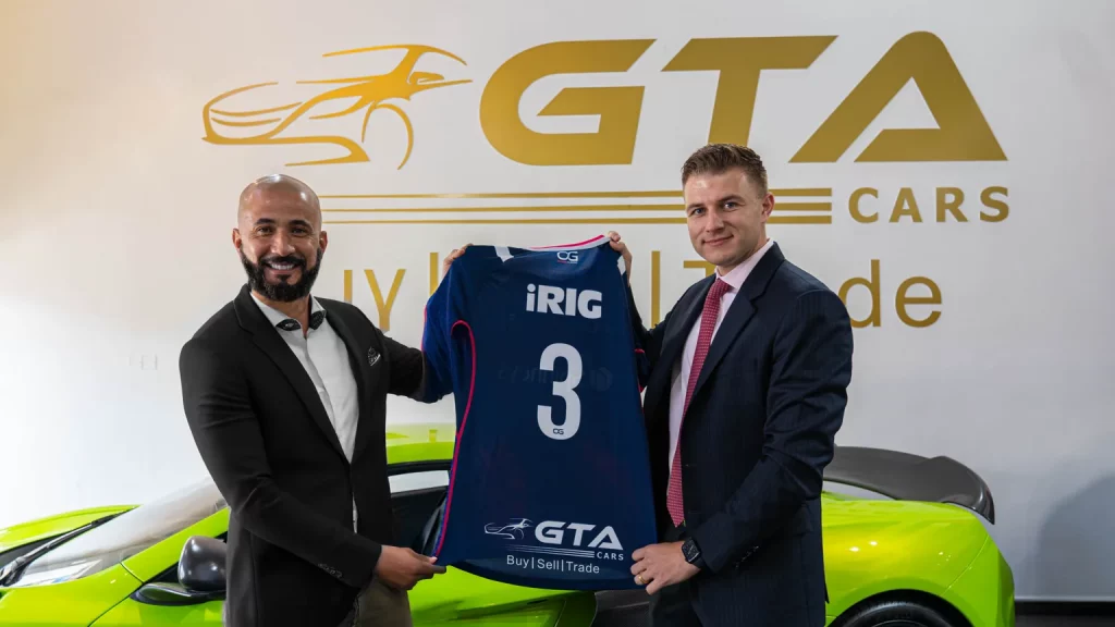 Band of Misfits rugby jersey number 3, carrying the GTA Cars logo, held up by two men at the GTA Cars showroom to mark the 2024 sponsorship.