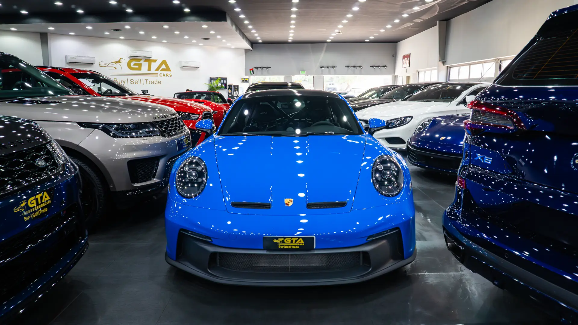 Blue Porsche 911 GT3 leading a line of pre-owned cars in the GTA Cars Dubai showroom